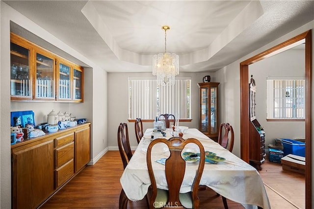 dining space with hardwood / wood-style flooring, an inviting chandelier, and a tray ceiling