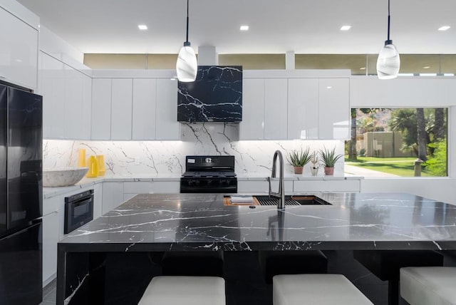 kitchen with white cabinets, a kitchen island with sink, dark stone countertops, and black appliances