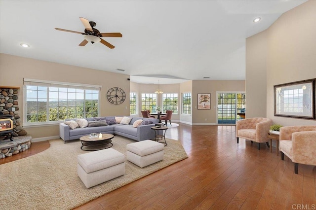 living room featuring ceiling fan with notable chandelier, plenty of natural light, a wood stove, and wood-type flooring