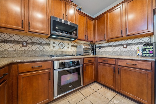 kitchen with light stone countertops, decorative backsplash, appliances with stainless steel finishes, and light tile patterned floors