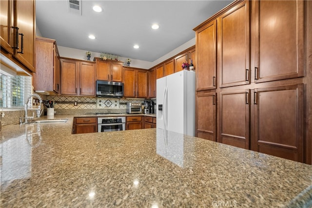 kitchen with kitchen peninsula, tasteful backsplash, light stone countertops, sink, and stainless steel appliances