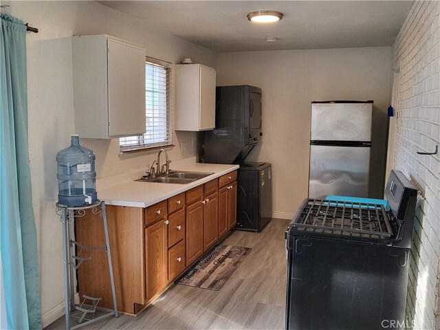 kitchen featuring stacked washer and clothes dryer, black range with gas cooktop, sink, light hardwood / wood-style floors, and stainless steel refrigerator