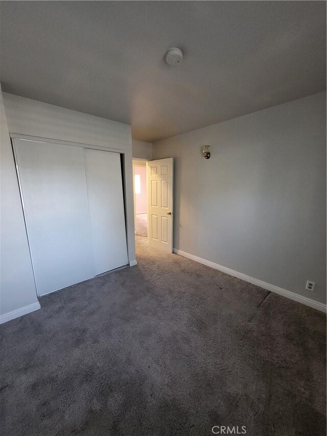 unfurnished bedroom with dark colored carpet and a closet