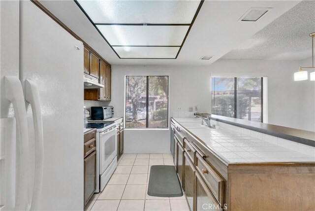 kitchen with tile counters, white appliances, light tile patterned flooring, hanging light fixtures, and sink