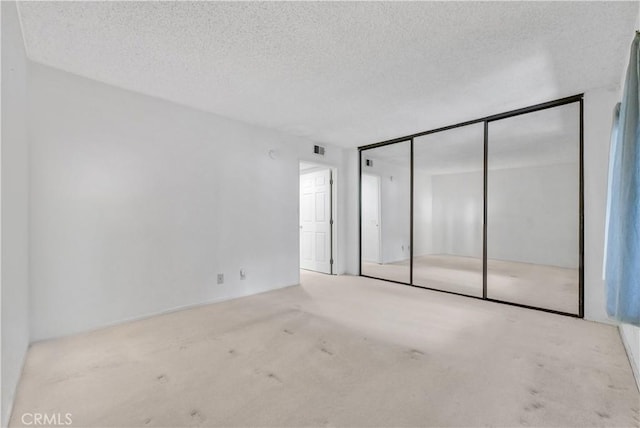 unfurnished bedroom featuring light colored carpet, a textured ceiling, and a closet