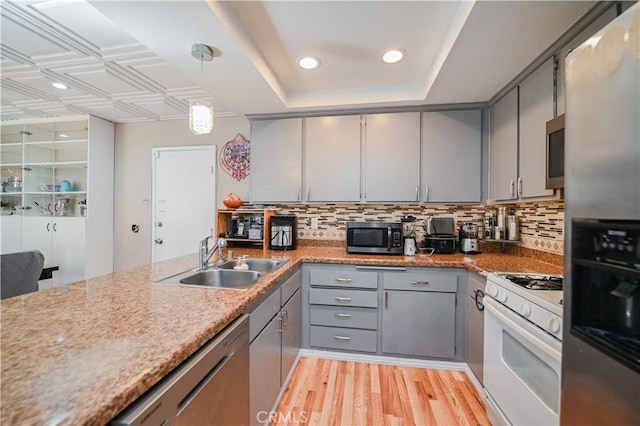 kitchen with sink, light hardwood / wood-style flooring, appliances with stainless steel finishes, tasteful backsplash, and decorative light fixtures