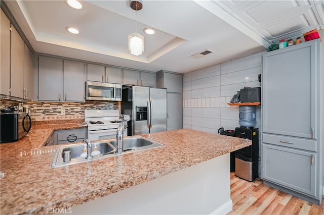 kitchen featuring a raised ceiling, kitchen peninsula, hanging light fixtures, and appliances with stainless steel finishes