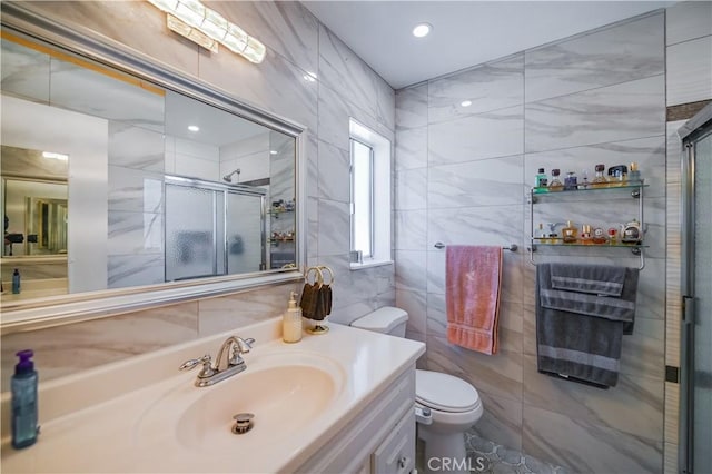 bathroom with a shower with door, vanity, tile walls, and toilet