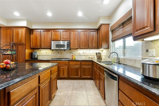 kitchen with appliances with stainless steel finishes, brown cabinets, a sink, and dark stone counters