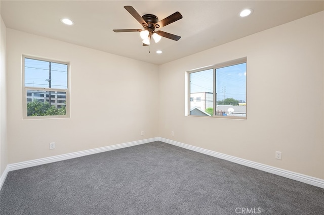 unfurnished room featuring dark carpet, a healthy amount of sunlight, and ceiling fan