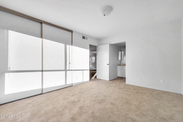 unfurnished bedroom featuring light carpet and ensuite bathroom