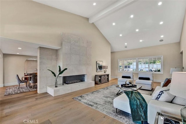 living room featuring a tile fireplace, light hardwood / wood-style floors, high vaulted ceiling, and beamed ceiling