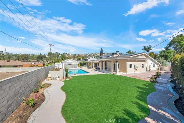 rear view of house featuring solar panels, a patio, a fenced in pool, and a lawn