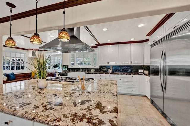 kitchen with built in fridge, white cabinets, wall chimney exhaust hood, decorative light fixtures, and light stone counters