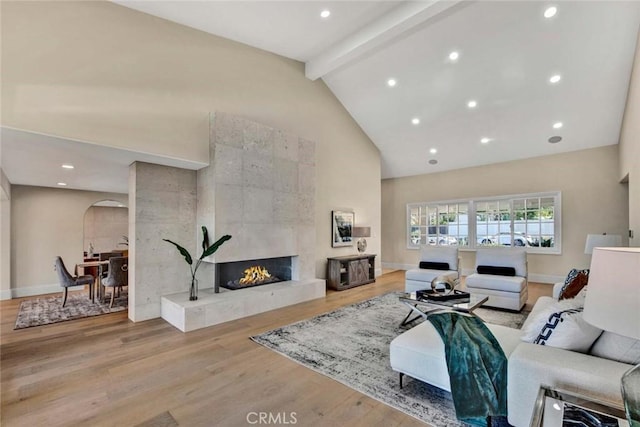 living room with beamed ceiling, light hardwood / wood-style floors, high vaulted ceiling, and a tiled fireplace