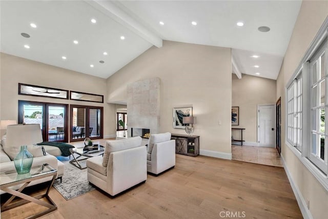 living room featuring beamed ceiling, high vaulted ceiling, light hardwood / wood-style flooring, and a healthy amount of sunlight