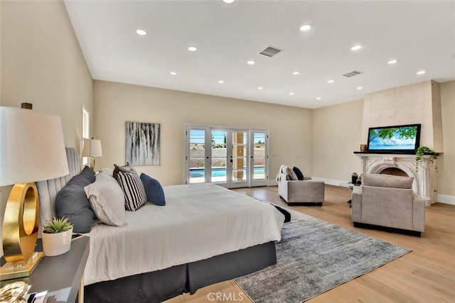 bedroom with access to exterior, french doors, a large fireplace, and light hardwood / wood-style flooring