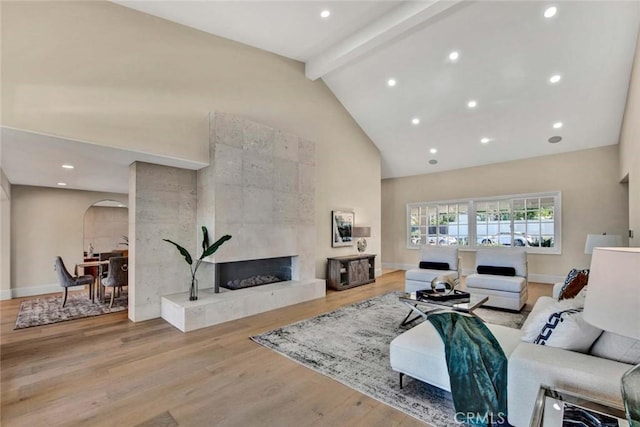 living room with beam ceiling, light wood-type flooring, high vaulted ceiling, and a tiled fireplace