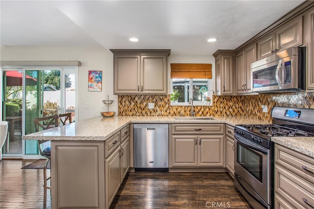 kitchen with kitchen peninsula, dark hardwood / wood-style flooring, a kitchen breakfast bar, sink, and stainless steel appliances