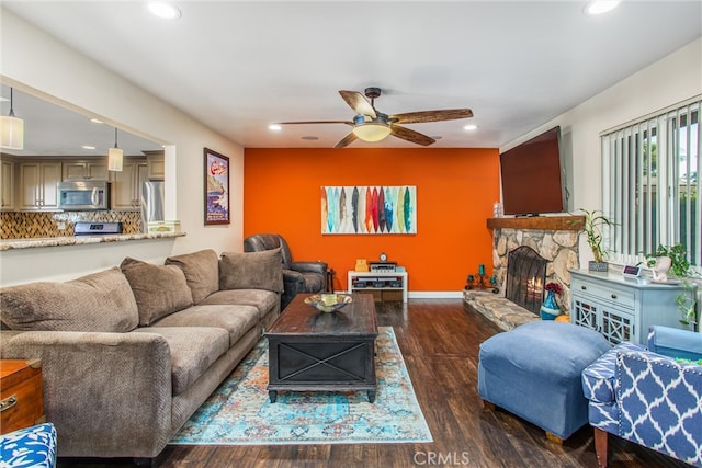 living room featuring a stone fireplace, dark hardwood / wood-style floors, and ceiling fan