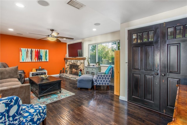 living room featuring a stone fireplace, ceiling fan, and dark hardwood / wood-style flooring