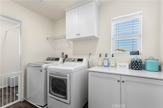 clothes washing area featuring dark wood-type flooring, washer and clothes dryer, and cabinets