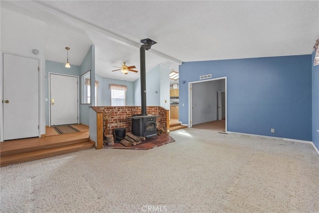 living area with a textured ceiling, visible vents, baseboards, vaulted ceiling, and a wood stove