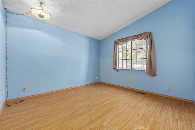 spare room featuring light wood finished floors, baseboards, visible vents, lofted ceiling, and a textured ceiling