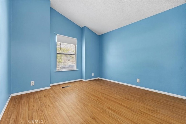 unfurnished room featuring a textured ceiling, wood finished floors, visible vents, baseboards, and vaulted ceiling