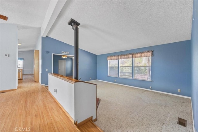 unfurnished room featuring visible vents, vaulted ceiling with beams, a textured ceiling, and baseboards