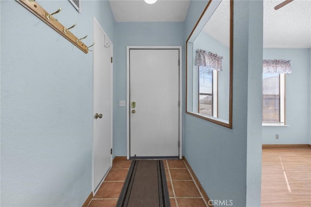 doorway to outside with light tile patterned flooring, a textured ceiling, and baseboards