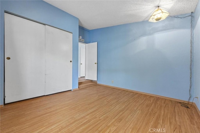 unfurnished bedroom featuring a textured ceiling, a closet, wood finished floors, and baseboards