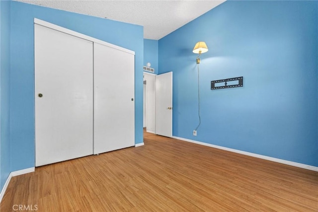 unfurnished bedroom with vaulted ceiling, a closet, wood finished floors, and baseboards