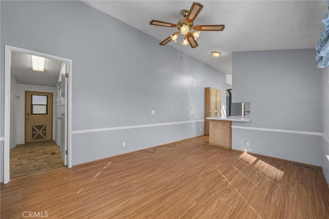 unfurnished living room with a textured ceiling, vaulted ceiling, light wood-type flooring, and a ceiling fan