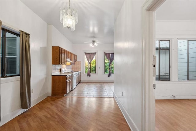 kitchen with decorative light fixtures, white gas range oven, decorative backsplash, light wood-type flooring, and ceiling fan with notable chandelier