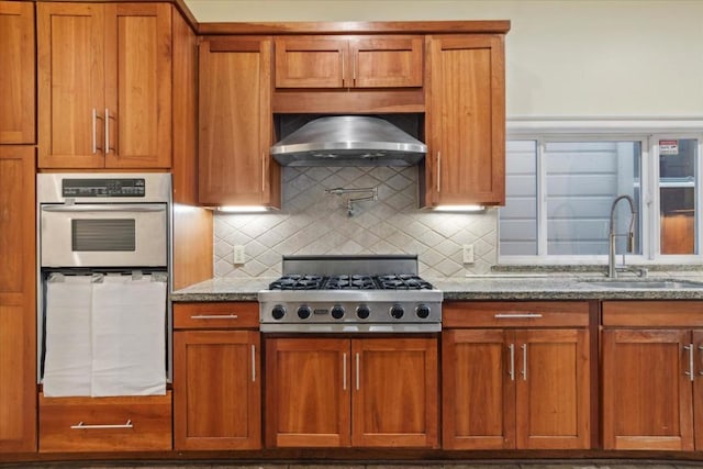 kitchen with light stone counters, sink, wall chimney range hood, and tasteful backsplash