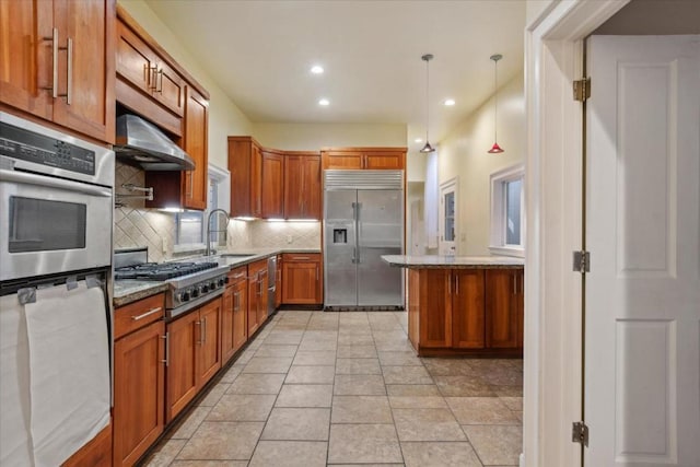 kitchen with stainless steel appliances, tasteful backsplash, decorative light fixtures, light stone countertops, and sink