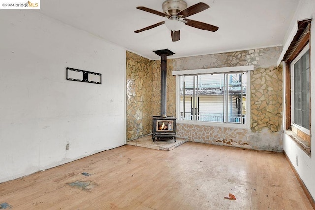 unfurnished living room with ceiling fan, a wood stove, and light hardwood / wood-style flooring