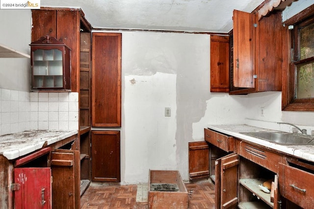 kitchen featuring tasteful backsplash, dark parquet flooring, light stone counters, and sink