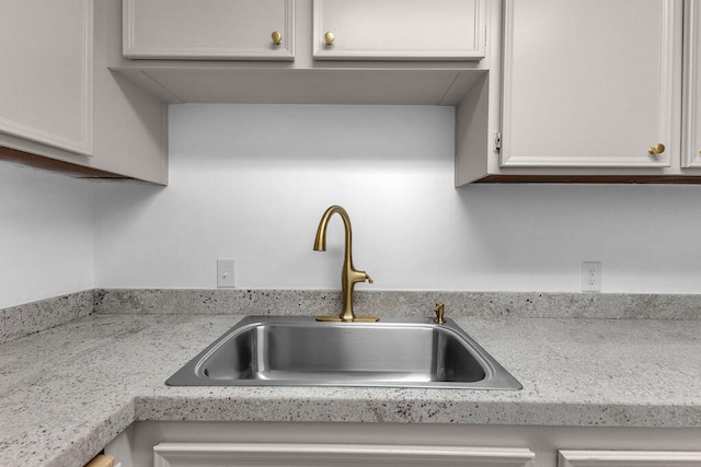 interior details with white cabinetry, light stone countertops, and sink