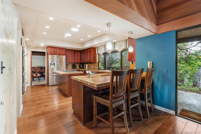 kitchen with wood counters, stainless steel refrigerator with ice dispenser, pendant lighting, light hardwood / wood-style floors, and a kitchen island