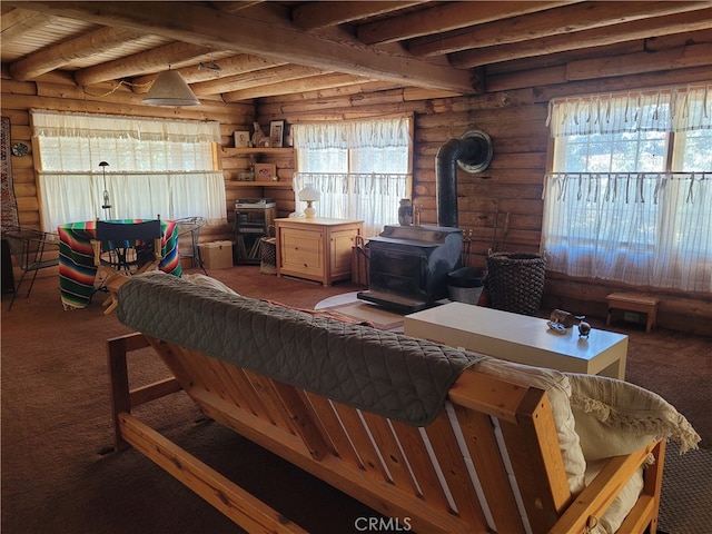 carpeted living room with log walls, beamed ceiling, a wood stove, and plenty of natural light