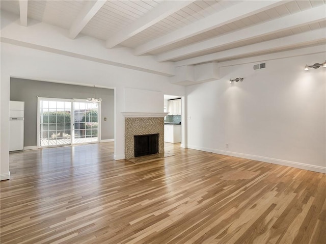 unfurnished living room featuring hardwood / wood-style flooring, a notable chandelier, beamed ceiling, and a tile fireplace