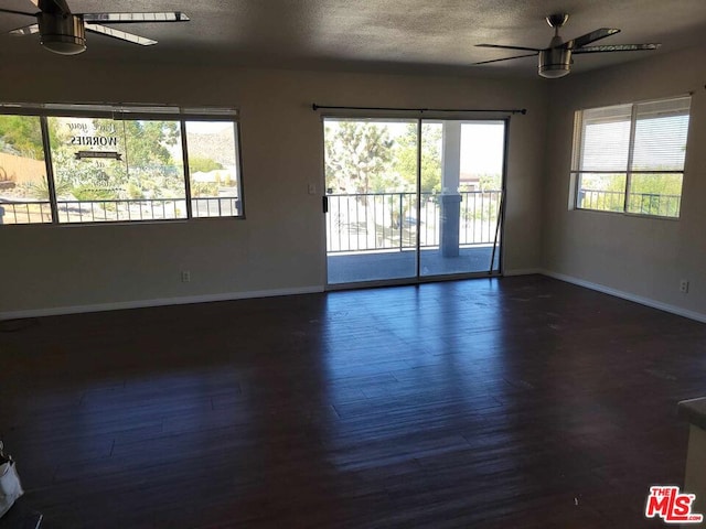 spare room with a textured ceiling, plenty of natural light, and dark hardwood / wood-style floors