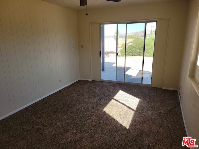 carpeted spare room with a textured ceiling, wooden walls, and ceiling fan