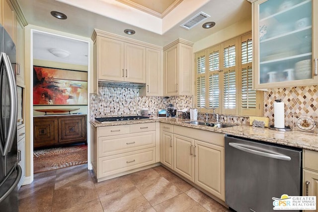 kitchen with cream cabinets, light stone counters, backsplash, appliances with stainless steel finishes, and sink