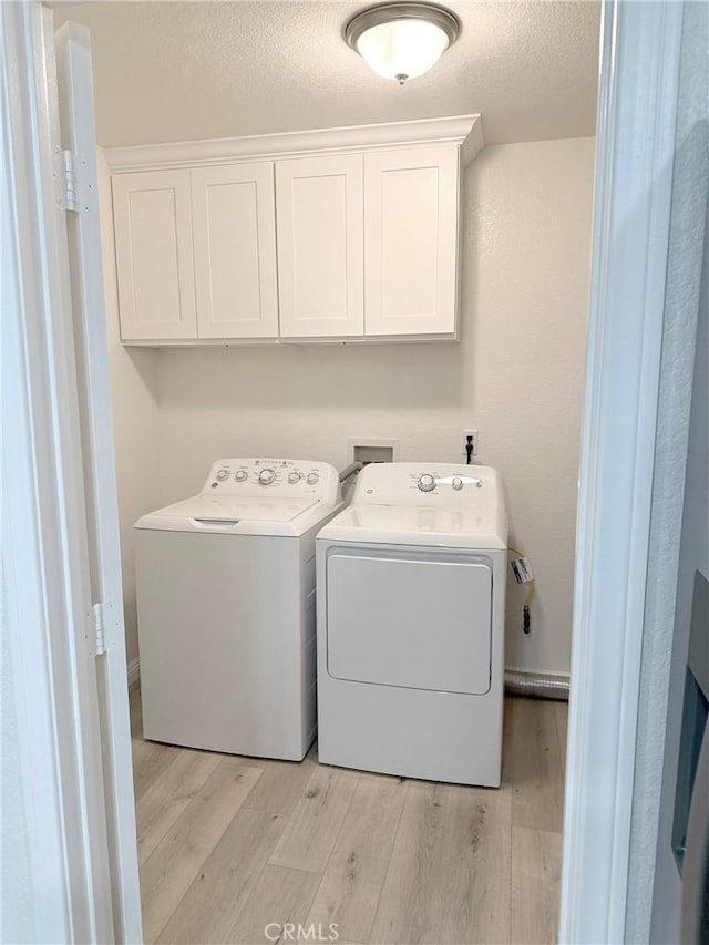 clothes washing area with cabinets, a textured ceiling, washing machine and dryer, and light hardwood / wood-style flooring