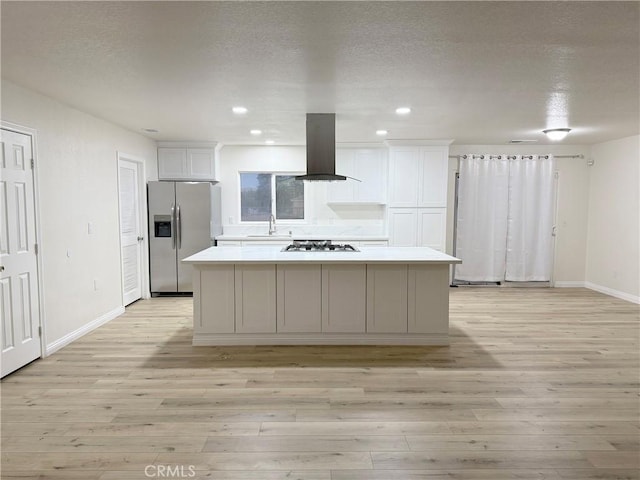 kitchen with light hardwood / wood-style flooring, white cabinets, wall chimney range hood, and appliances with stainless steel finishes