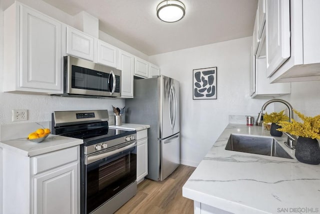 kitchen featuring sink, stainless steel appliances, light stone countertops, light hardwood / wood-style floors, and white cabinets