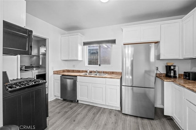 kitchen featuring washing machine and clothes dryer, white cabinetry, sink, appliances with stainless steel finishes, and light wood-type flooring